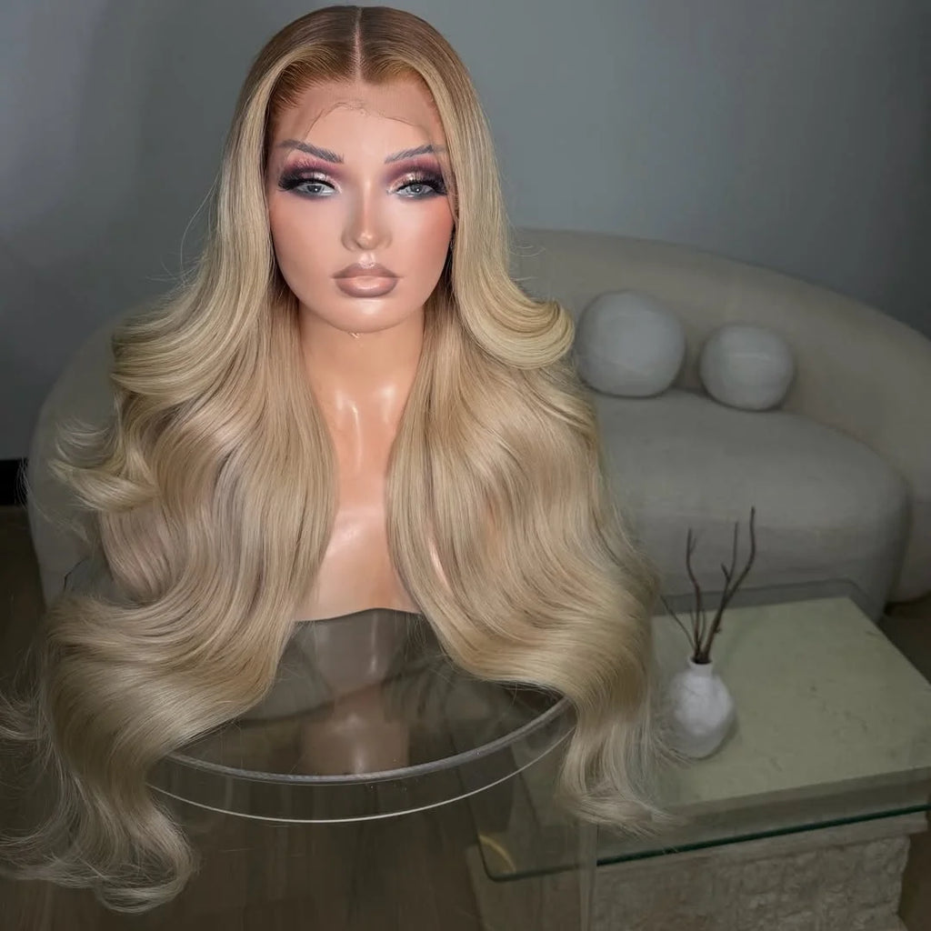 Long, wavy blonde wig with a center part displayed on a mannequin bust in an indoor setting with a sofa and glass table in the background.
