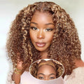 A woman wearing a full wig with tight, glossy curls in a warm brown and blonde ombré color. A circular inset at the bottom shows a close-up of the wig's lace front and hair texture.