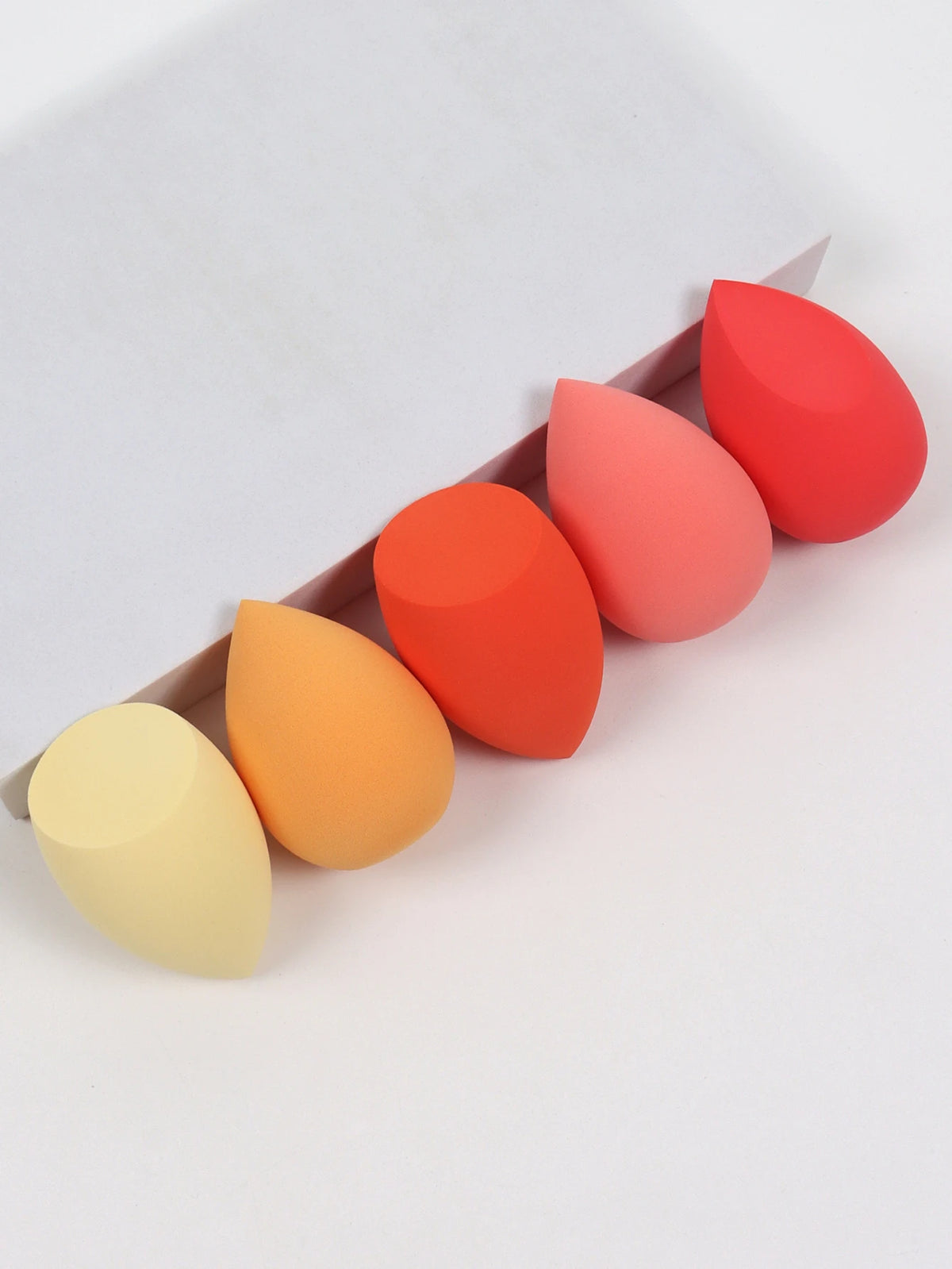 Set of colorful makeup sponges in a brown box on a white background