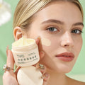 Woman applying cream from a TWG jar to her face with a green background
