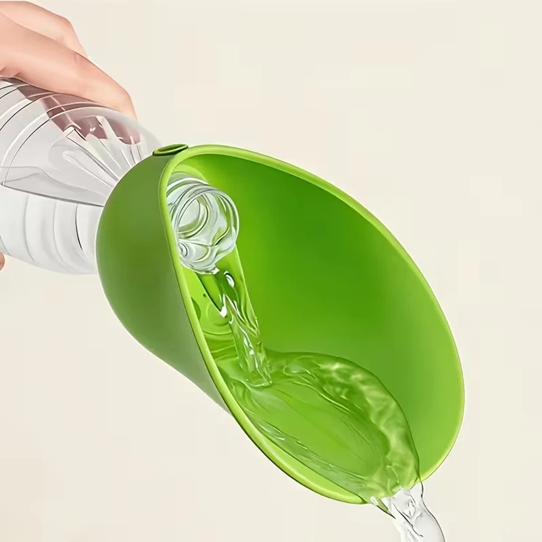 A bright green silicone funnel being used to pour clear water from a clear plastic bottle, held by a hand against a plain light beige background.