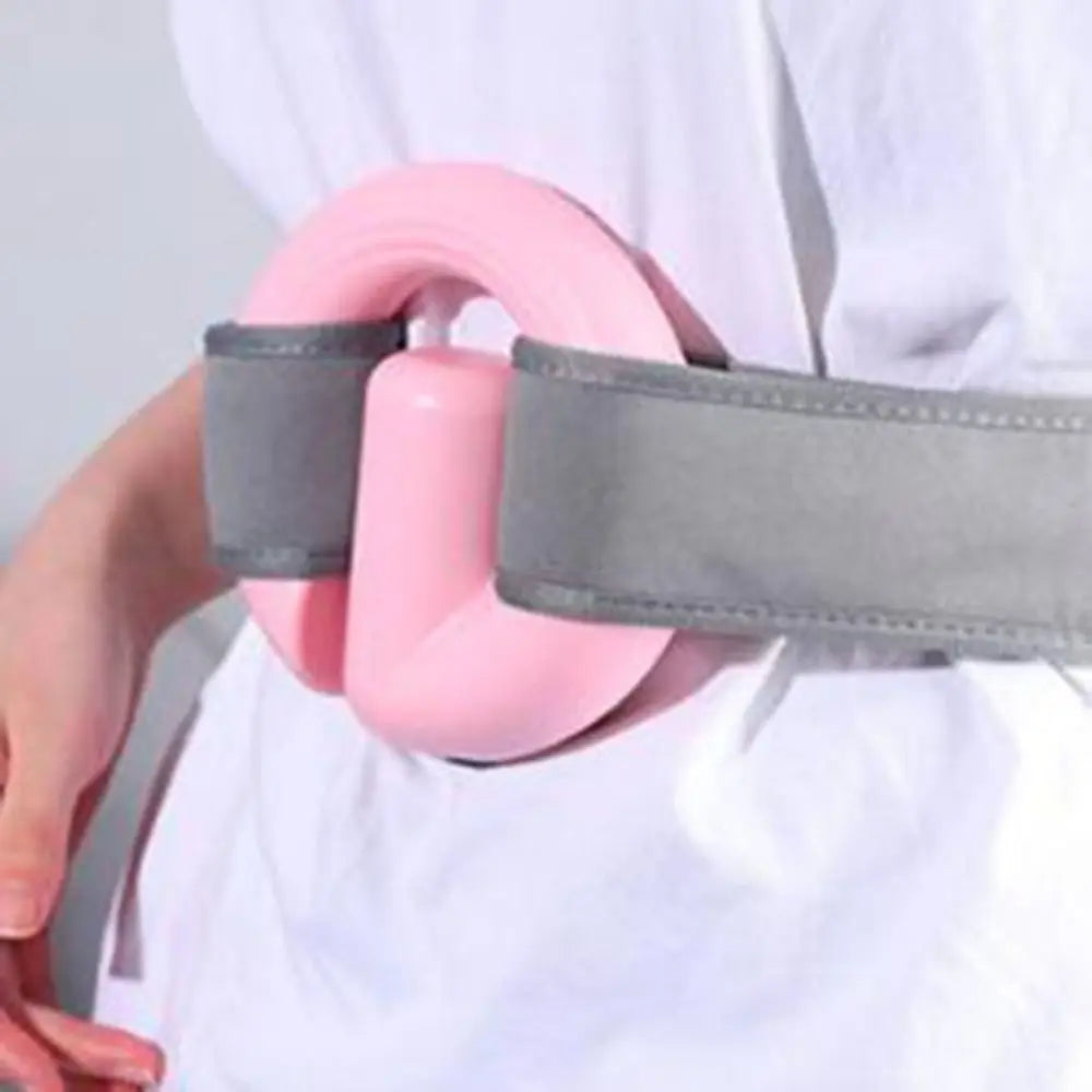 A close-up of a person wearing a pink pelvic floor trainer with gray straps around the waist, shown against a white shirt.