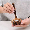 Wooden massage roller held by two hands against a neutral background