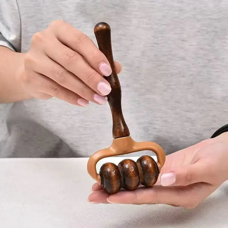 Wooden massage roller held by two hands against a neutral background