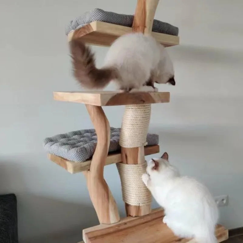A wooden cat tree with cushioned platforms and a rope-wrapped scratching post, shown indoors with two cats interacting with it. One cat stands on a middle platform, and another sits on the base looking up.