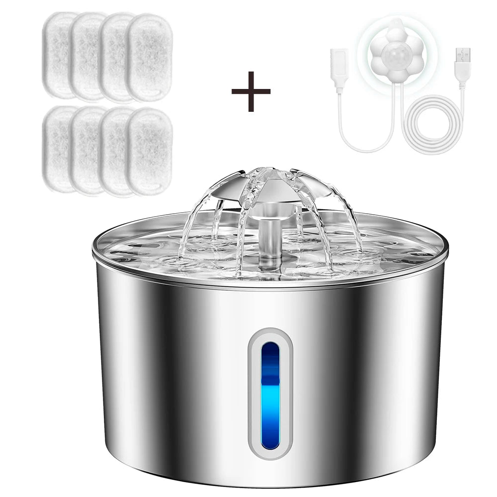 A stainless steel pet water fountain with a water fountain nozzle spraying water, shown with six white filter pads and a white USB charging cable on a white background.