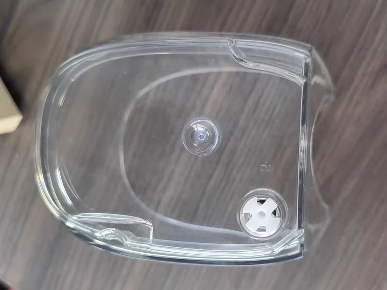 A clear plastic replacement cover or guard for a circular device, shown from a top-down view on a dark wood-grain surface.
