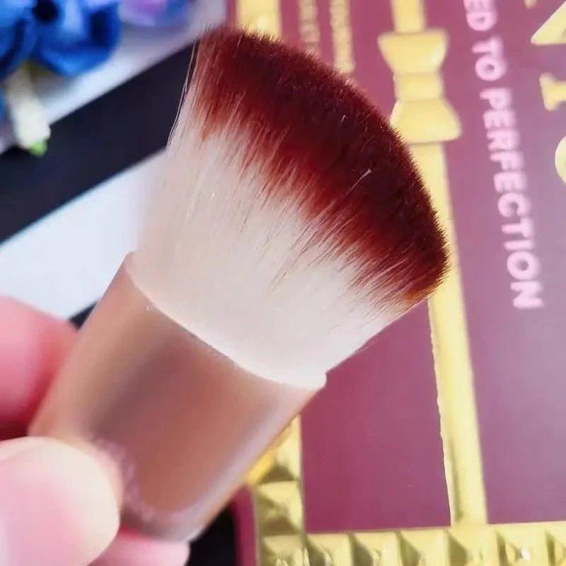 Makeup brush held by a hand with blurred product packaging in the background
