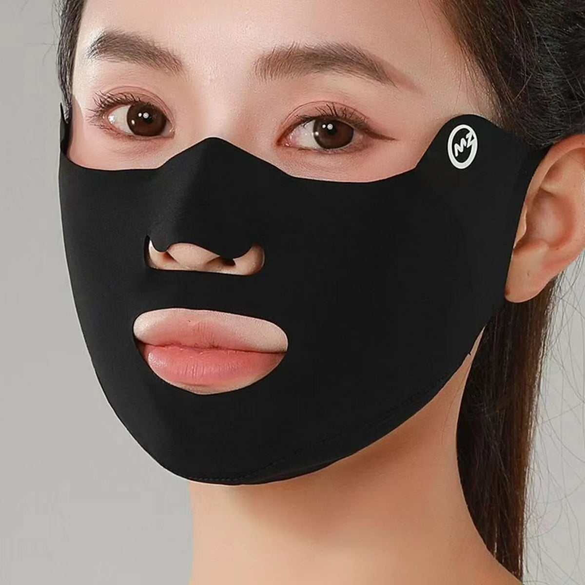Black face mask with cutouts for eyes, nose, and mouth worn by a person on a gray background