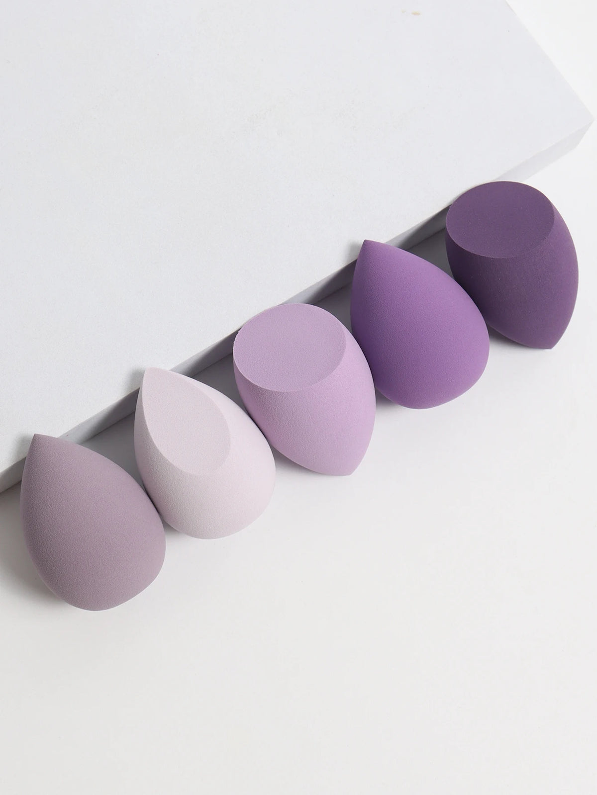 Set of purple and gray makeup sponges on a white background