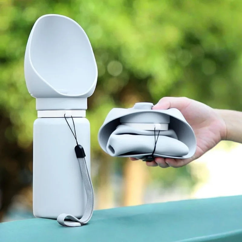 White collapsible dog water bottle folded and unfolded, held in hand outdoors