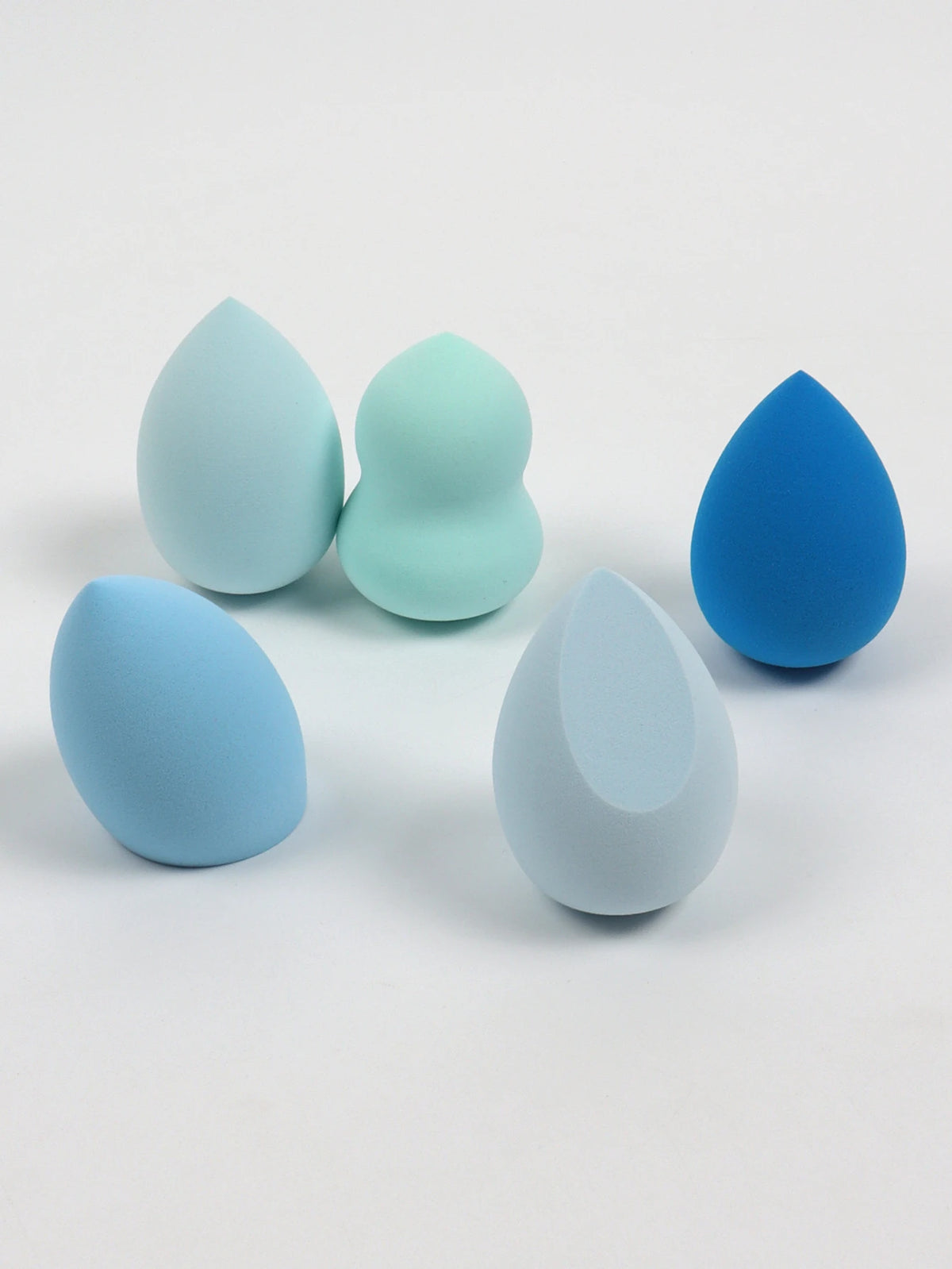 Set of five blue and green makeup sponges on a white background