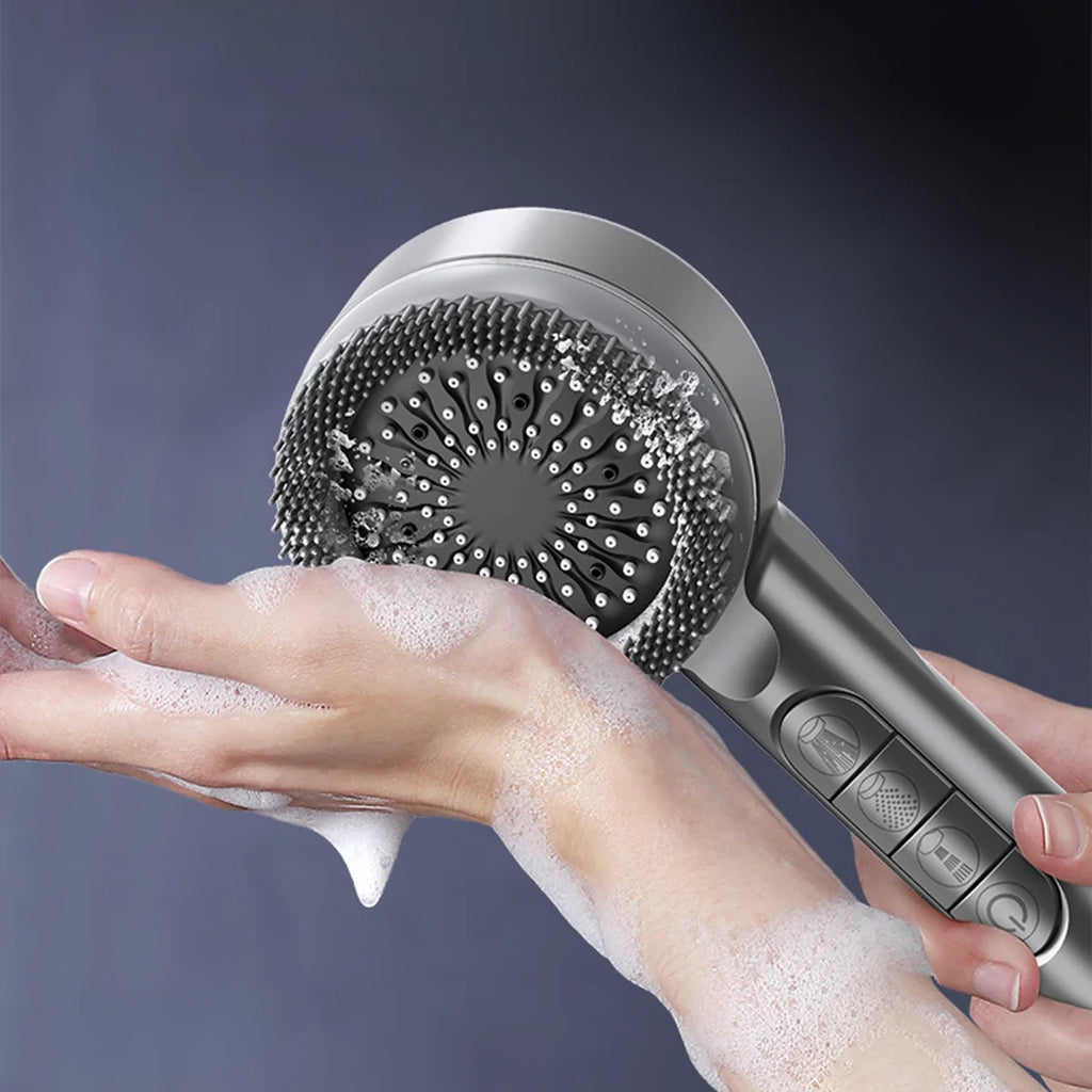 A handheld electric hand wash brush with a metallic gray body and bristled cleaning head, shown being used on a foamy hand against a dark blue-gray background.