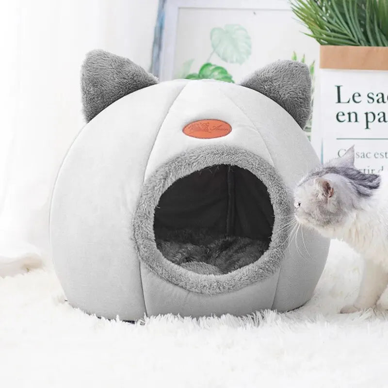 Cat-shaped pet bed with a cat peeking out from inside on a white surface.