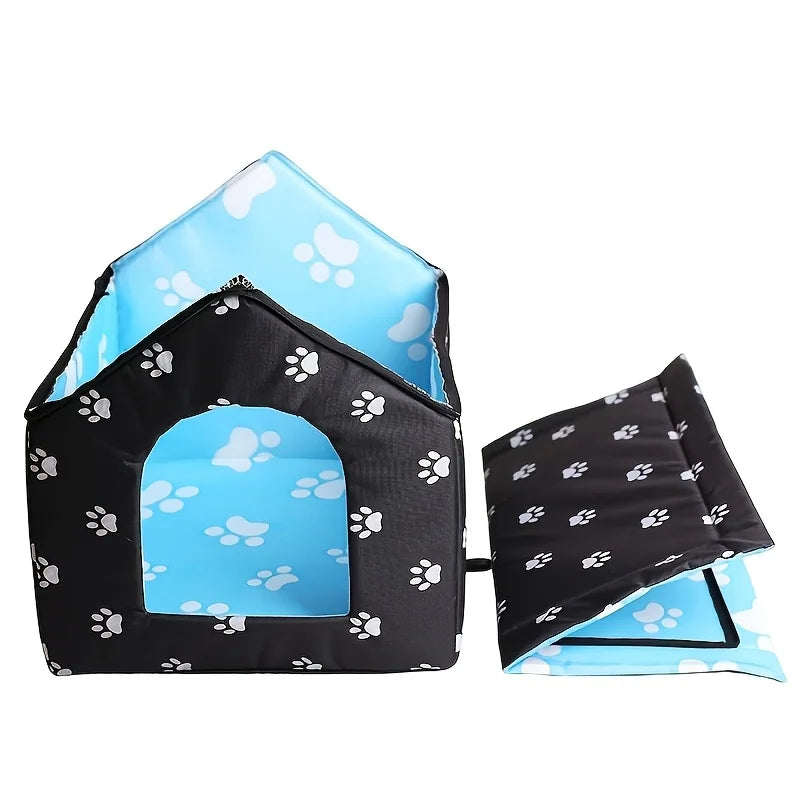 A house-shaped pet bed shown open and folded, with a black exterior covered in white paw prints and a light blue interior with white paw prints, on a plain white background.