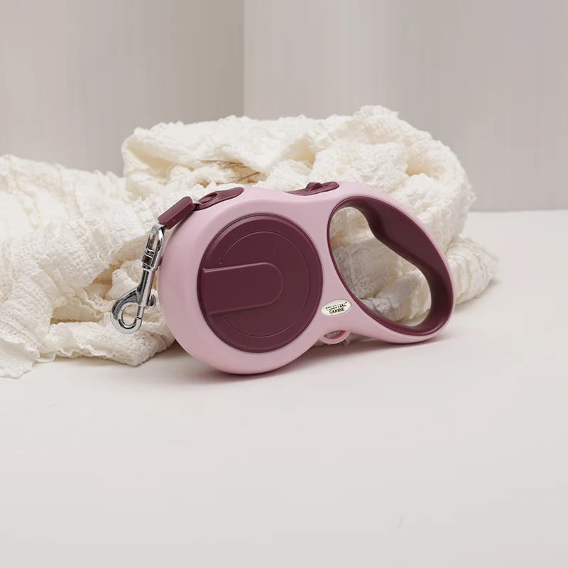 Pink and purple retractable dog leash on a white surface with a white blanket in the background
