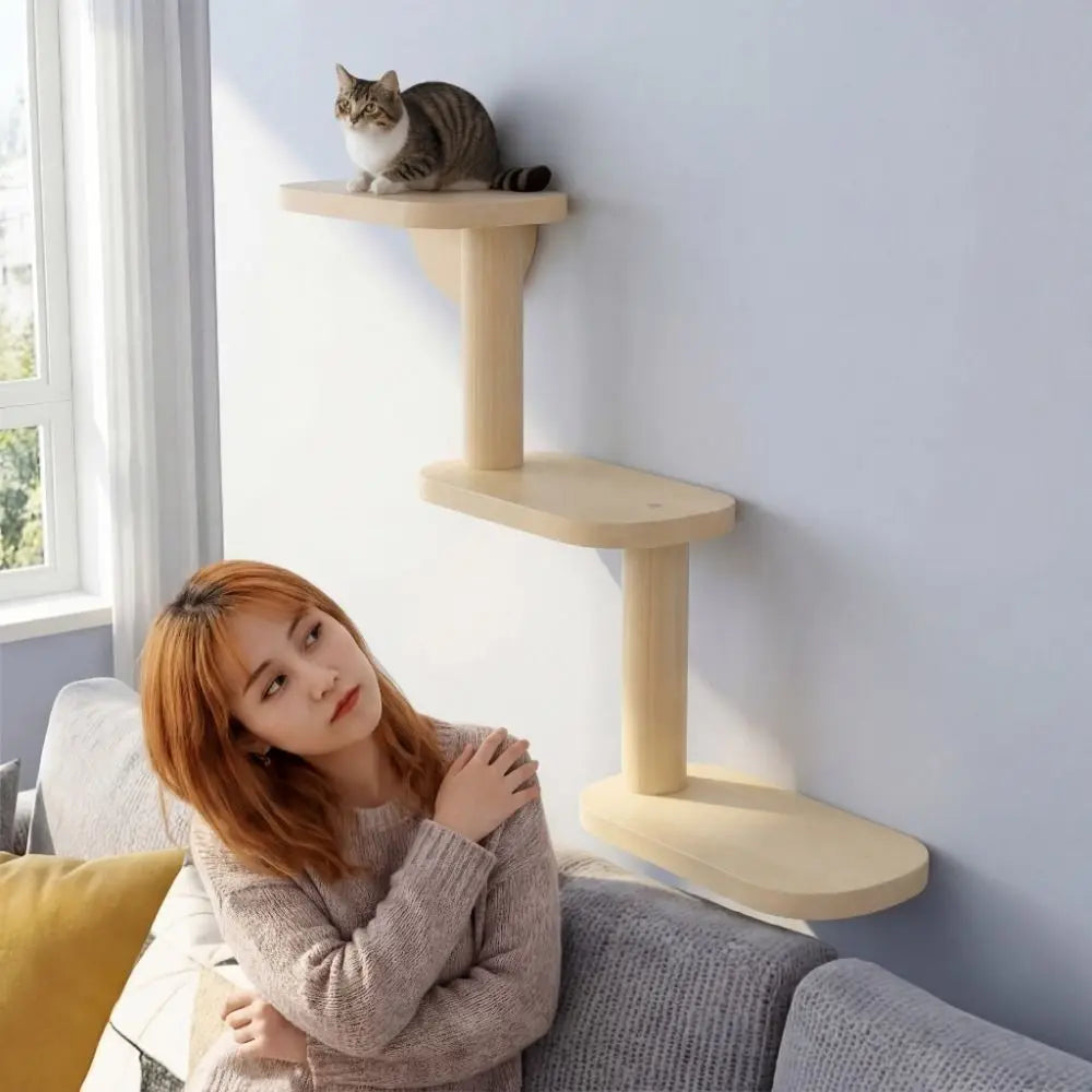 Woman sitting on a couch next to a wooden cat tree with a cat on top, in a bright room.
