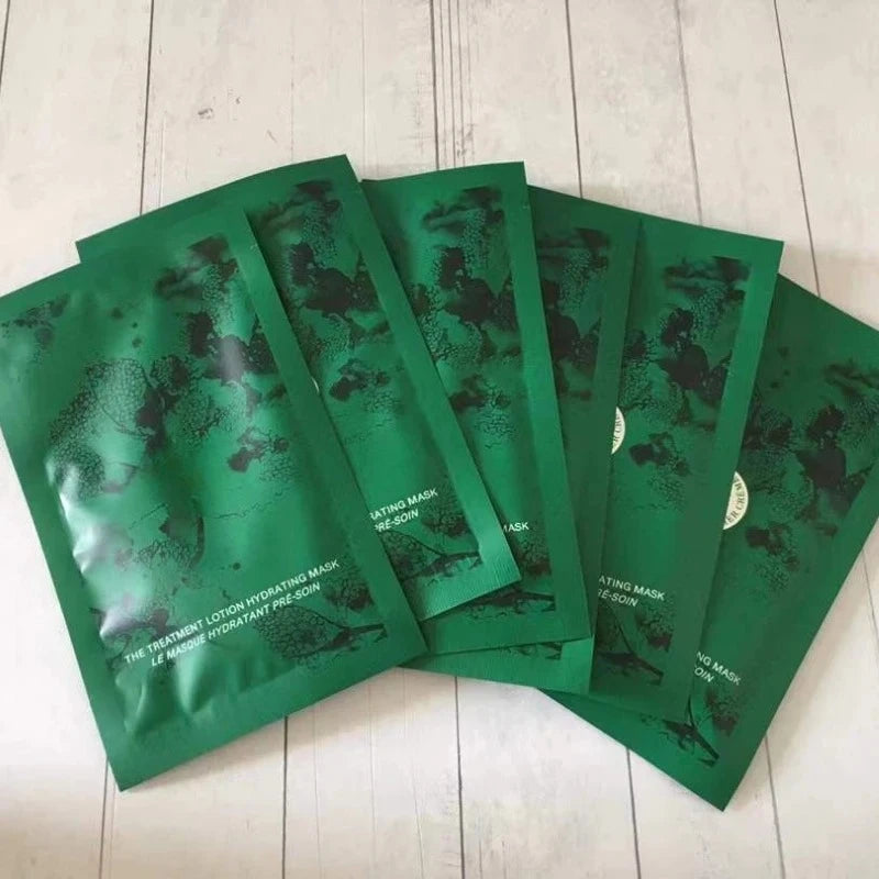 Five green skincare mask packets fanned out on a light wood surface. The packets feature a dark green abstract pattern and white text reading 'THE HYDRATING LOTUS HYALURONIC MASK'.