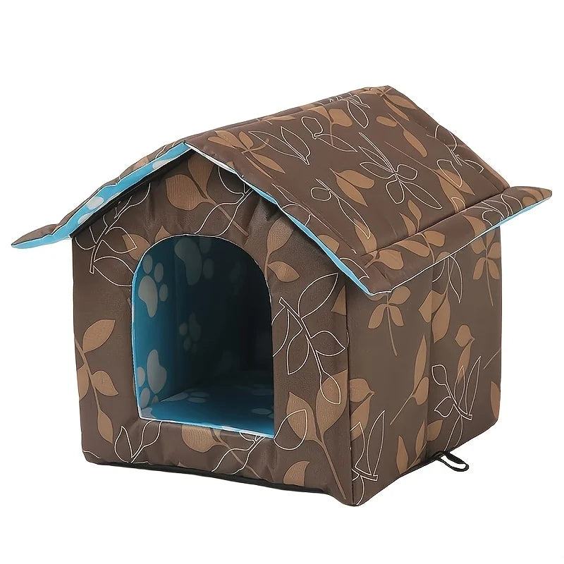 A small dog house pet bed with a brown and tan leaf patterned exterior, a blue interior, and light blue trim along the roof edge, shown on a plain white background.