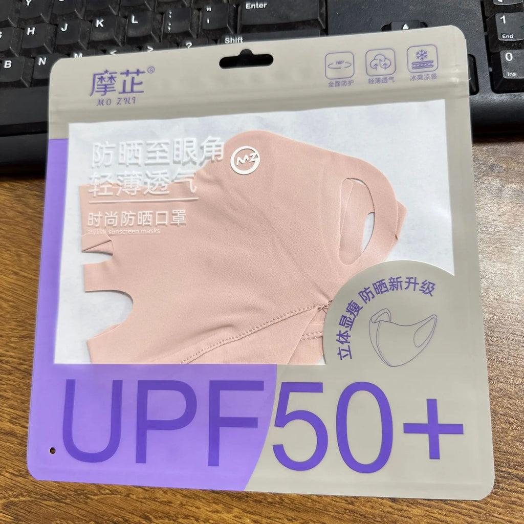 A packaged pink UV-blocking face mask with Chinese text and a large 'UPF50+' print on the front, photographed on a wooden surface with a keyboard in the background.
