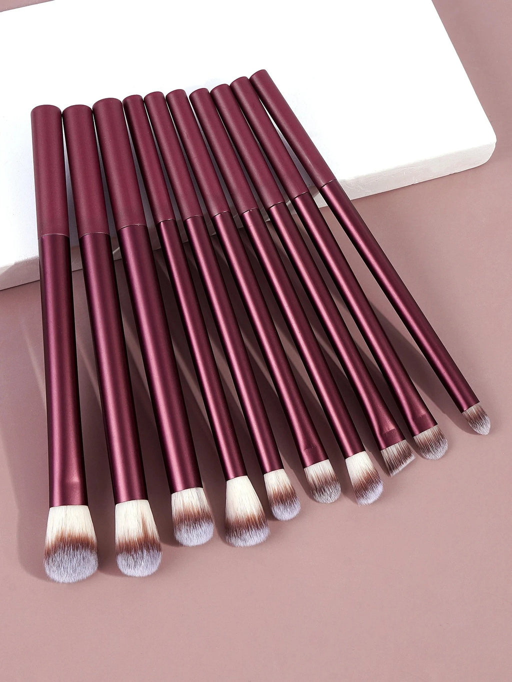 Set of makeup brushes with burgundy handles on a pink background