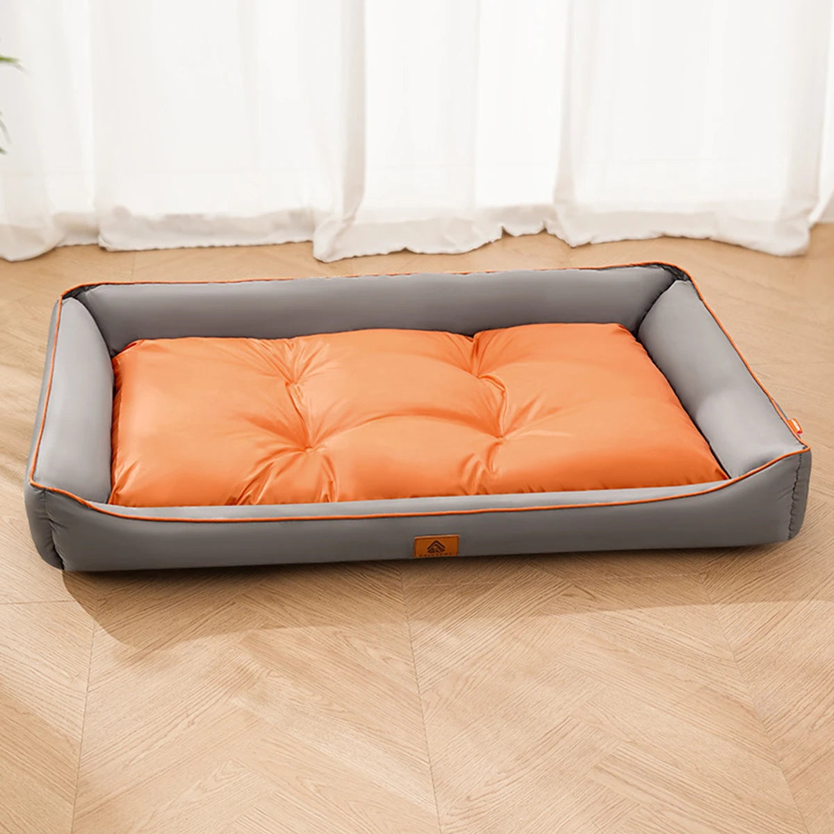 Gray and orange pet bed on a wooden floor with white curtains in the background