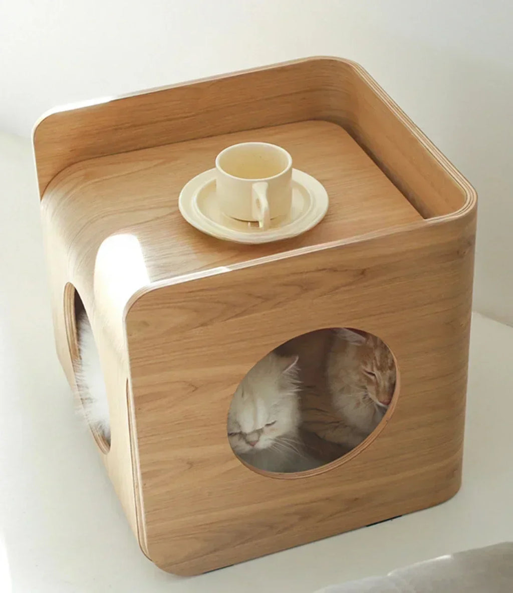 Wooden pet bed with a circular opening for cats, featuring two cats inside and a cup on top.