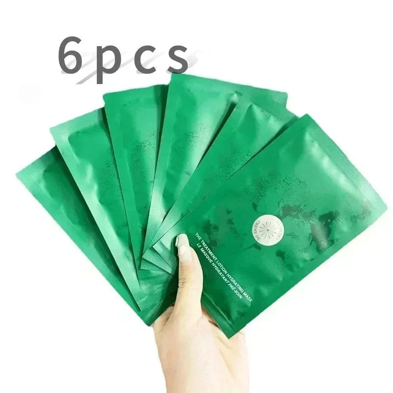 Hand holding six green facial mask packages with a white background