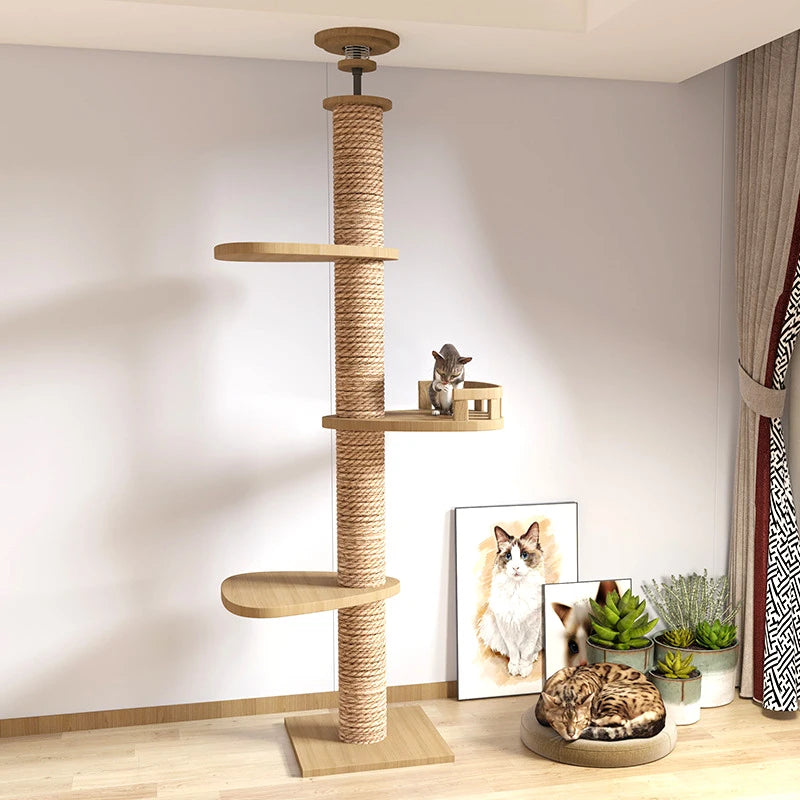 A tall wooden cat tree with a rope-wrapped post stands in a room corner against a light wall. The tree has three wooden perches and a small shelf holding a small cat.