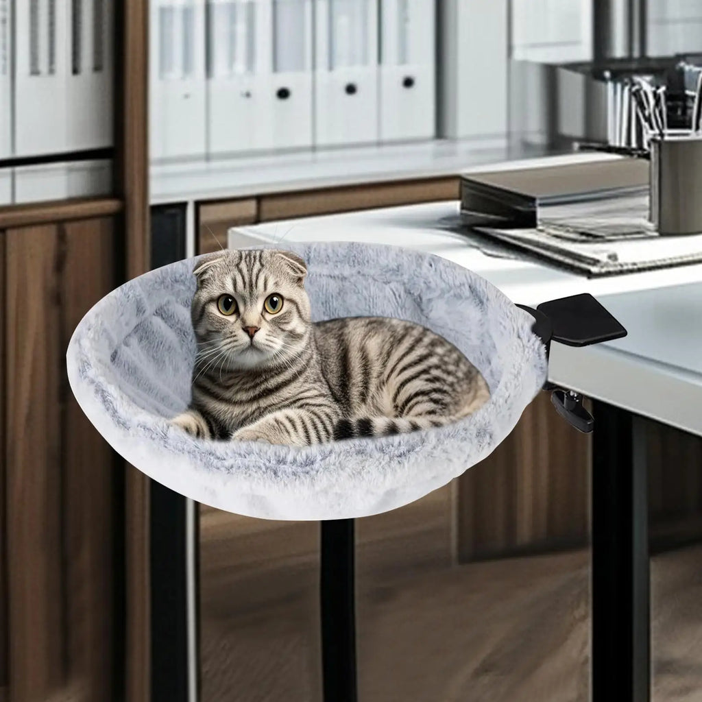 Cat sitting in a round pet bed attached to a desk in an office setting