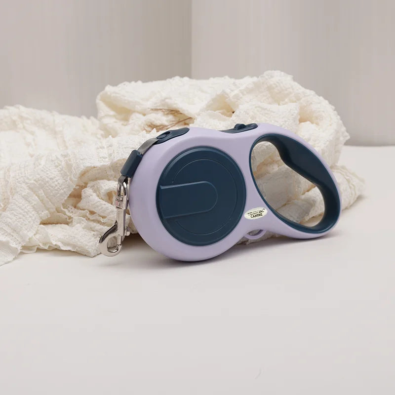Retractable dog leash with purple handle and blue reel on a white surface with white fabric.