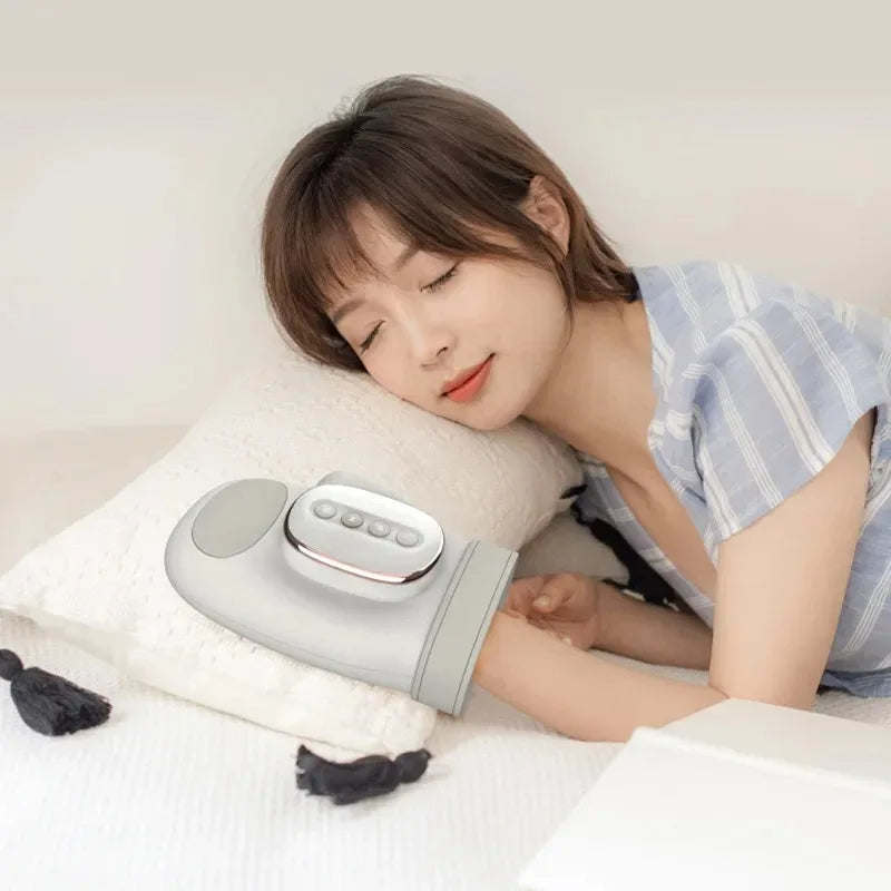 Woman using a handheld massager on her arm with a white pillow and light background