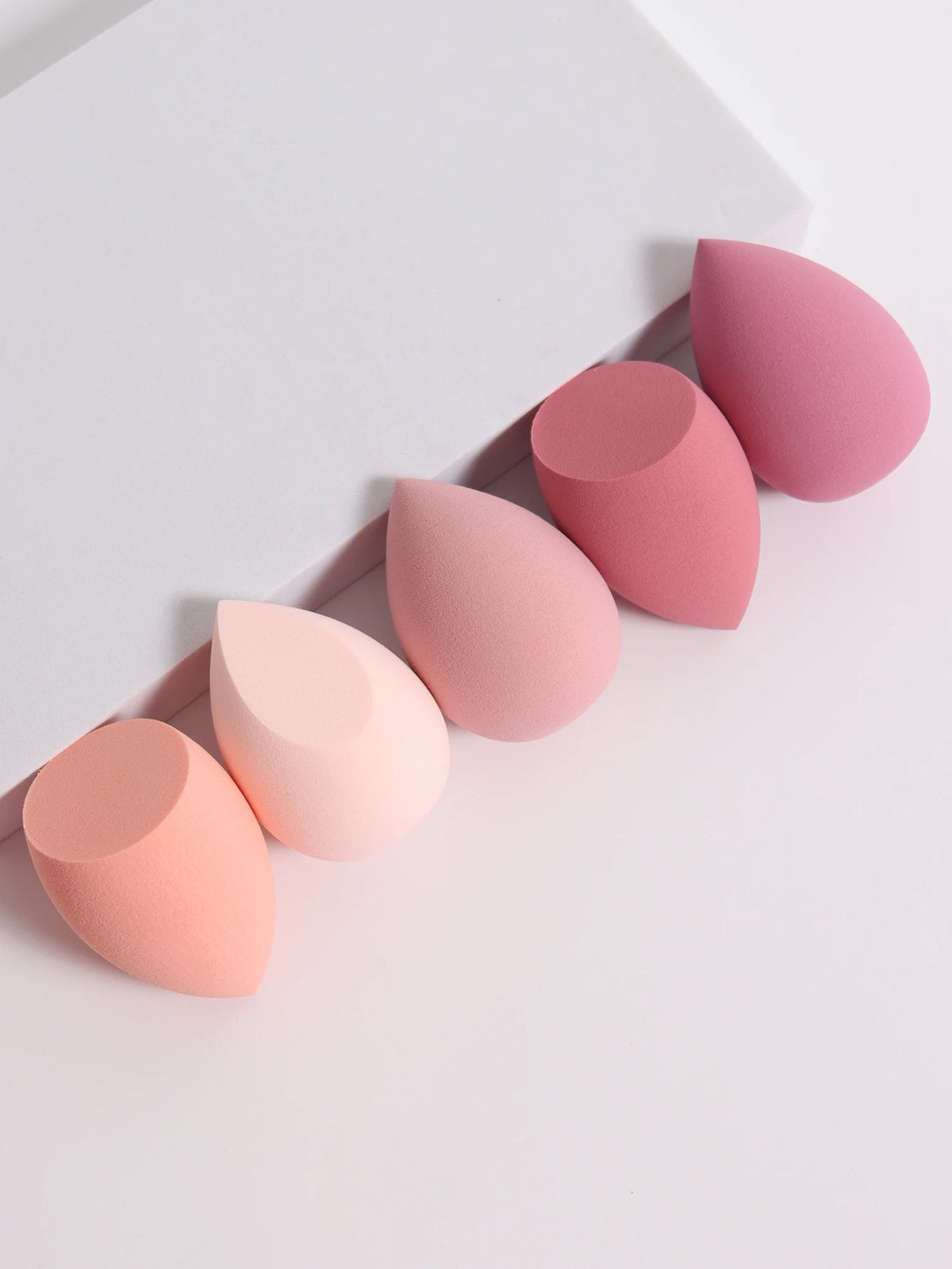 Set of pink and peach makeup sponges on a light gray background